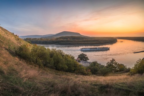 Panoramablick vom Ufer auf die Donau bei Bratislava während des Sonnenuntergangs. Ein Flussschiff fährt vorbei.