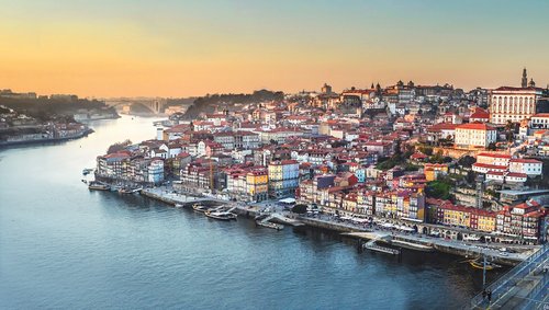 View of the old town of Porto on the Douro River at sunset with colorful houses and a bridge in the foreground.