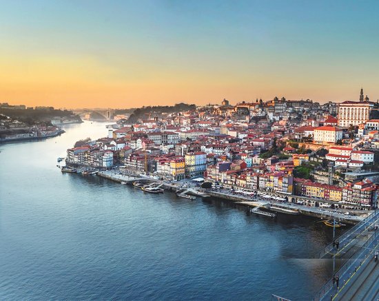 View of the old town of Porto on the Douro River at sunset with colorful houses and a bridge in the foreground.