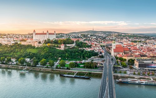 Panorama of Bratislava with the Danube and a bridge in the foreground. In the background, Bratislava Castle on a hill, surrounded by the city in good weather.