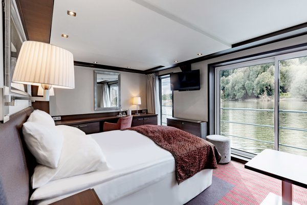 The junior suite on board the A-ROSA CLEA with double bed, seating area, floor-to-ceiling windows, and juliette balcony.