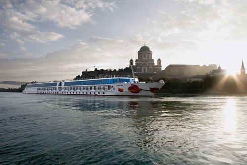 The river cruise ship A-ROSA MIA sails past Esztergom on the Danube with the St. Adalbert Cathedral at sunrise.