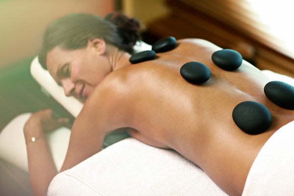 A woman lies on a massage table in the SPA-ROSA while hot stones are placed on her back.