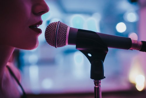 Close-up of a singer singing into a microphone, with a blurred background and blue lighting.