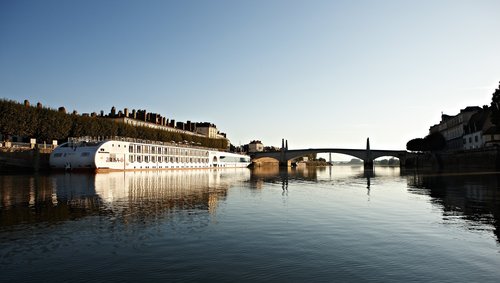 The A-ROSA STELLA is moored on the bank in a city on the Rhône at sunrise, with a bridge and buildings in the background.