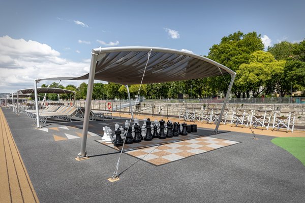 The sundeck with a large chessboard, sun loungers, and parasols in sunshine with a slightly cloudy sky.