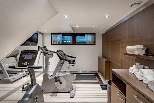 Modernly equipped fitness room with two cross trainers, mirror wall, wooden details, and towels on a shelf.
