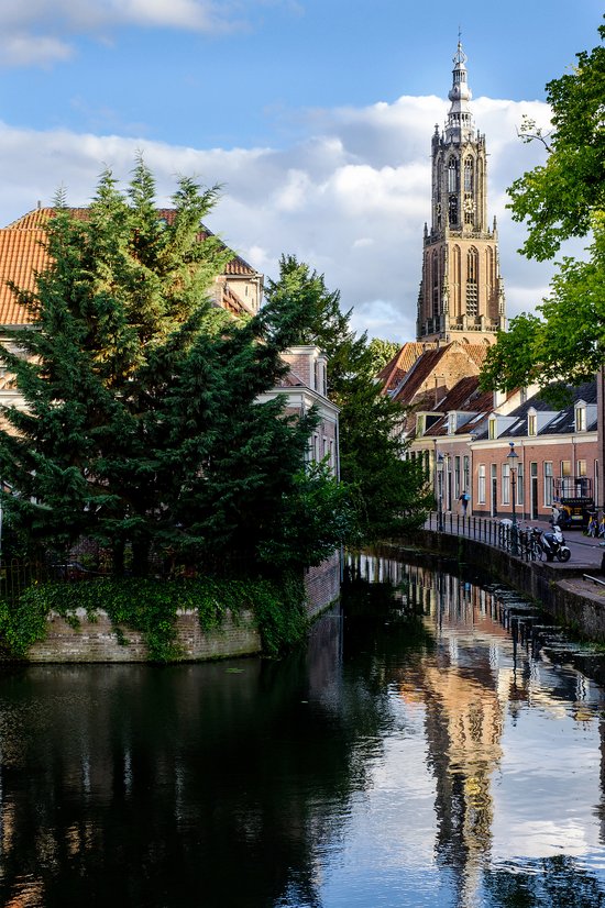 A canal in Utrecht, adorned with trees and buildings. A historic church with a tall tower in the background is reflected in the water.