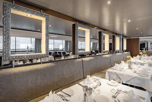 Stylishly set restaurant area of the A-ROSA ALEA with windows, floral decorations, and dimmed lighting.