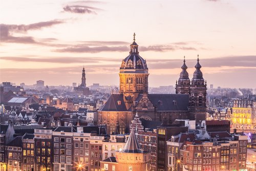 Evening city view of Amsterdam with historic buildings, illuminated streets, and a dramatic sky with clouds.
