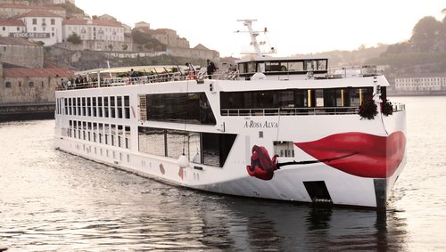 River cruise ship A-ROSA ALVA on the Douro in front of a city with historic buildings and red roofs.
