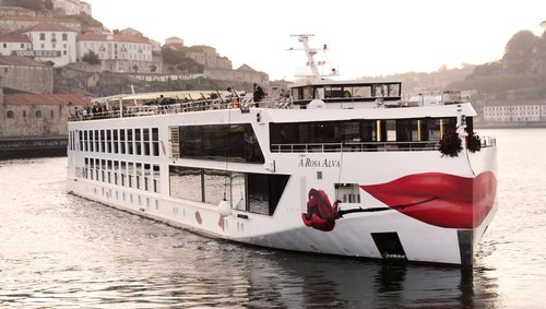 River cruise ship A-ROSA ALVA on the Douro in front of a city with historic buildings and red roofs.