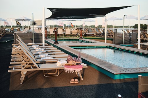 The sun deck of the A-ROSA SENA in daylight with a swimming pool and kids pool as well as numerous deck chairs.