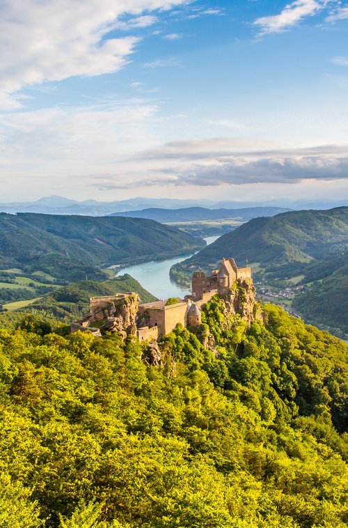 View of the ruins of a castle in the green hilly landscape of the Wachau with the Danube in the background under a cloudy sky