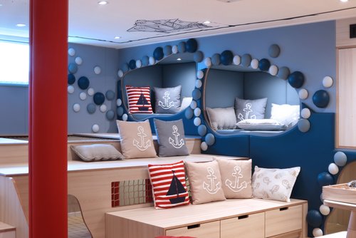 A-ROSA Kids Club with blue walls, seating areas with anchor and sailboat cushions, round wall decorations, and wooden stairs with storage space
