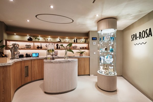 Reception area of the SPA-ROSA with decorative shelves, marble counter, and glass display case with products next to a staircase.