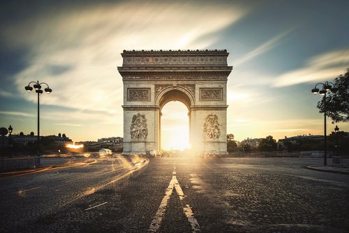 Sunset behind the Arc de Triomphe in Paris with light trails on the street.