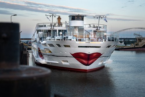 The A-ROSA SENA with a painted kissing mouth and rose on the bow is docked in the evening at a port, the sky is slightly cloudy.