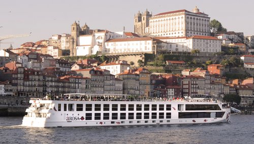 River cruise ship A-ROSA ALVA on the Douro in front of a city with historic buildings and red roofs.