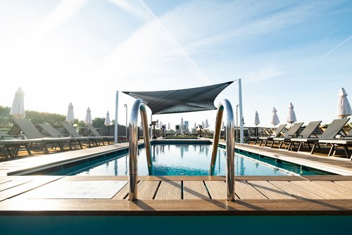 Pool on the sun deck of the A-ROSA SENA with metal railing and deck chairs with white sun parasols under a clear sky