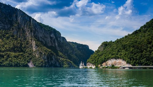 Blick auf die Katarakten im Donau Delta mit steilen bewaldeten Felsen und einer Kirche am Ufer unter blauem Himmel