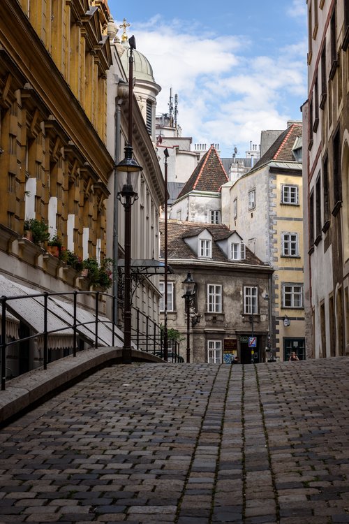 Die Griechengasse in Wien, eine schmale, gepflasterte Gasse mit historischen Gebäuden und Laternen, die eine charmante, altmodische Atmosphäre ausstrahlen. Copyright: Lisa Stelzel