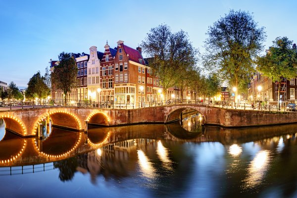Panorama von Amsterdams Grachten bei Abenddämmerung mit historischen Gebäuden und beleuchteten Brücken