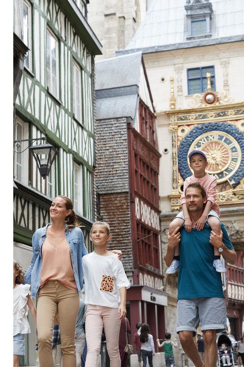 A family with two children strolls through the historic old town of Rouen with half-timbered houses and a large astronomical clock.