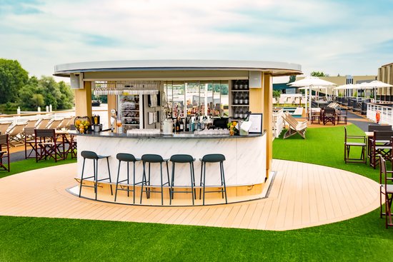 The sun deck of the A-ROSA SENA at dusk with the atmospherically lit UP & DOWN BAR and seating areas, view of the river and illuminated Amsterdam.